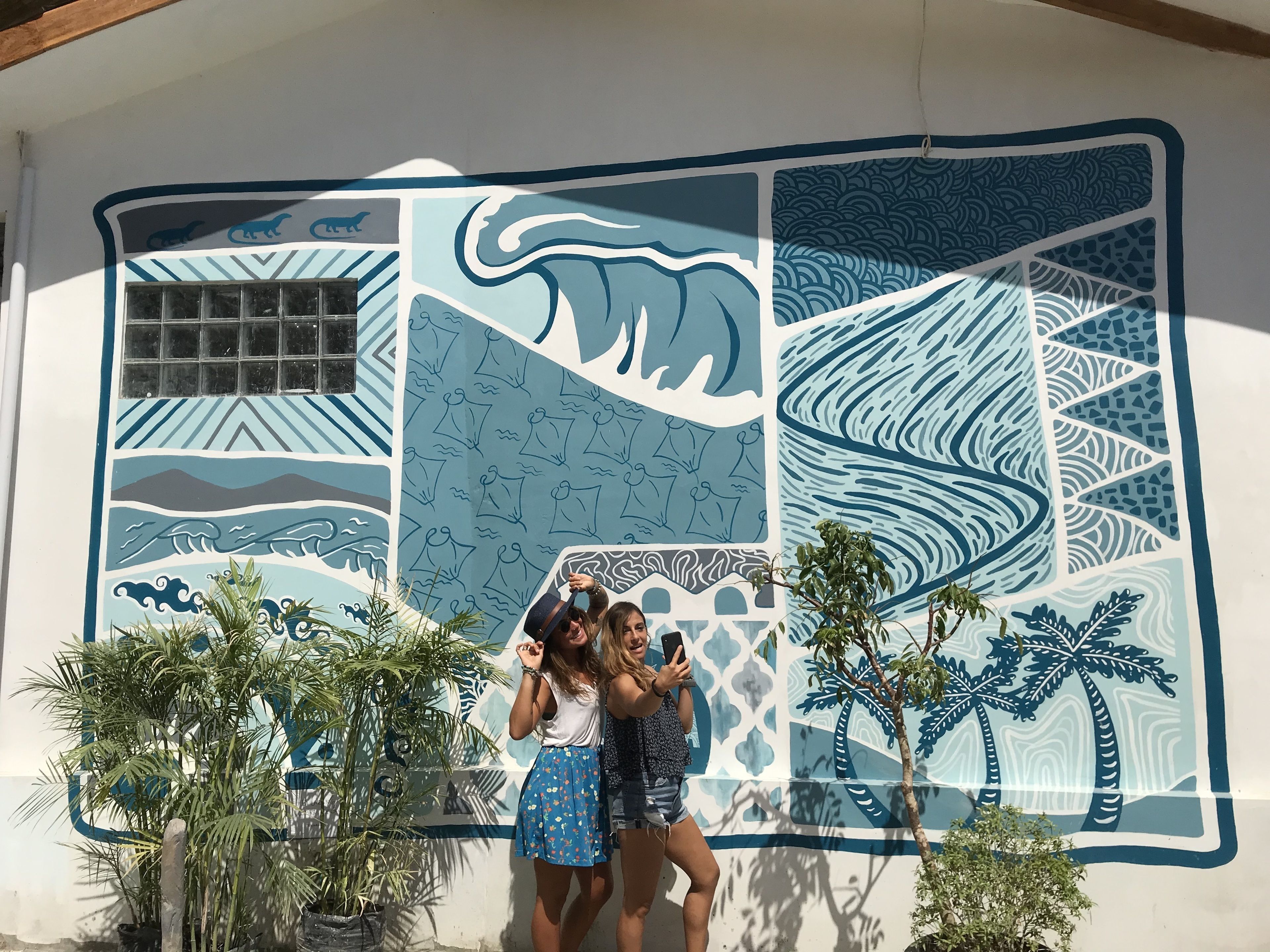 A mural with ocean and wave patterns, palm trees, and a grid-like window.