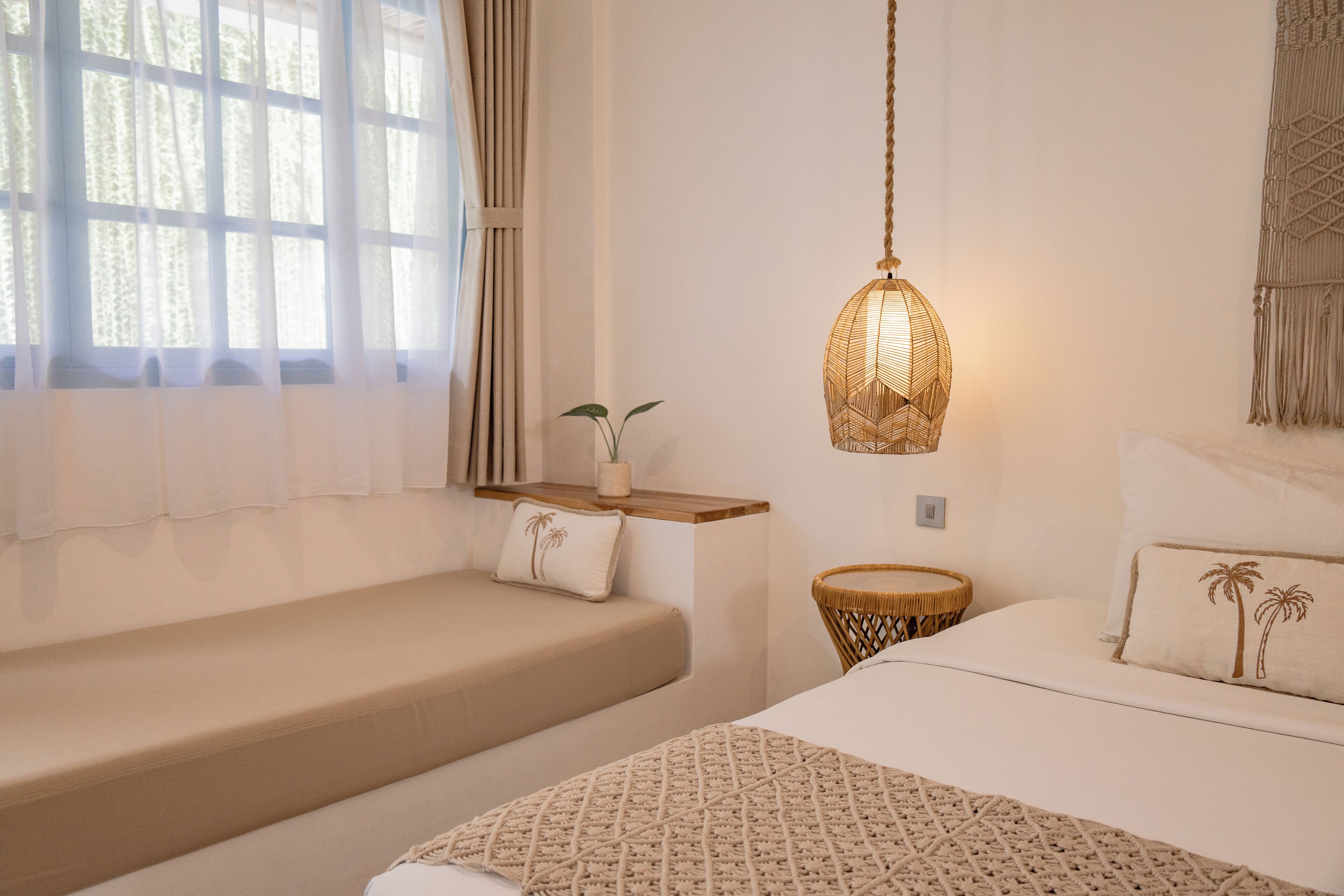A bedroom with a bed, two bedside tables, a hanging light fixture, and a window with curtains.