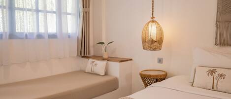 A bedroom with a bed, two bedside tables, a hanging light fixture, and a window with curtains.
