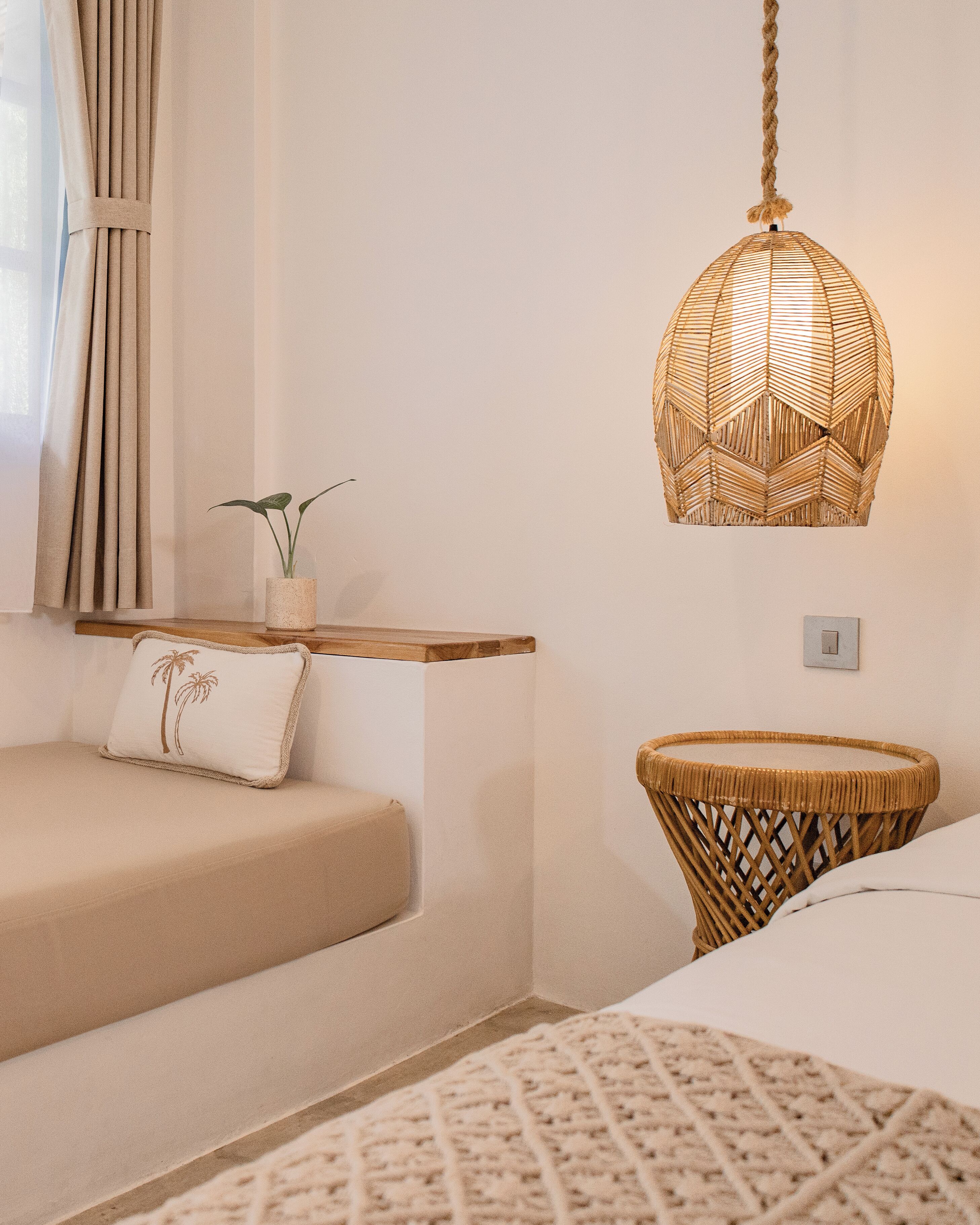 A room with a sofa, a small table with a plant, a woven basket, and a hanging light fixture.