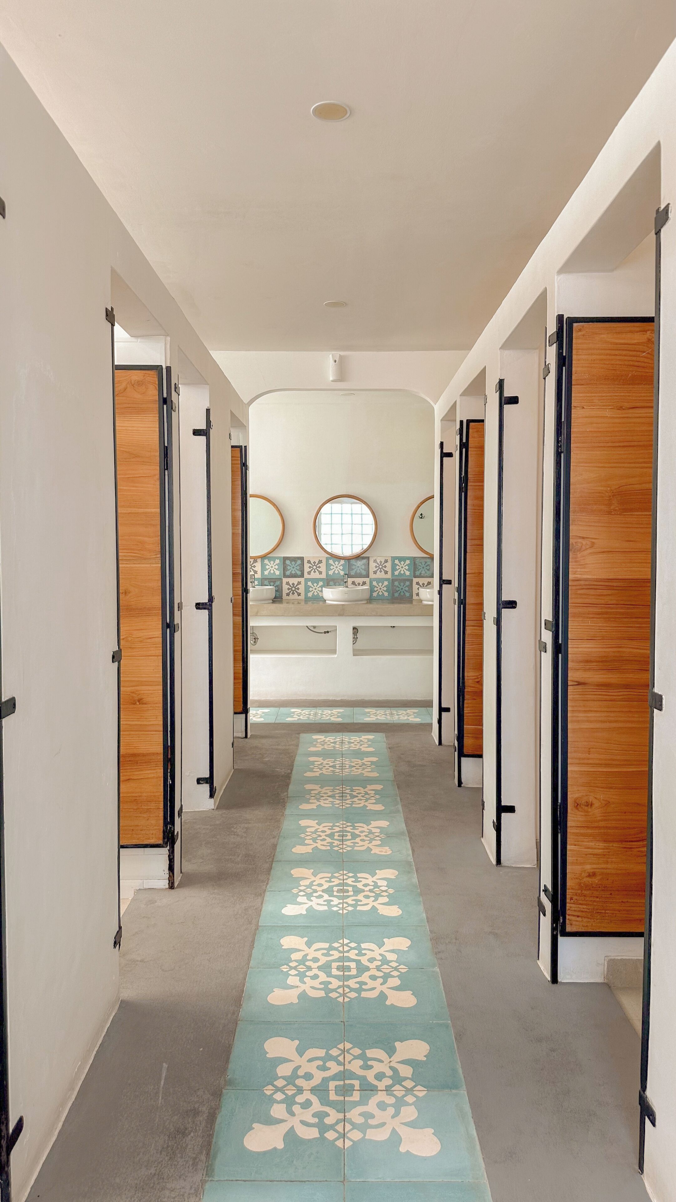 Un couloir doté d’un sol à motifs menant à une salle de bain avec deux lavabos et des miroirs.