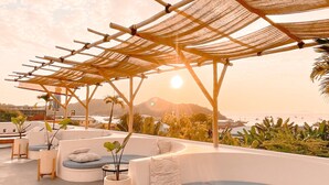 A rooftop terrace with a curved seating area, a small table, and a pergola structure.