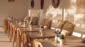 A sunlit dining area with wooden tables and chairs, a ceiling fan, and hanging light fixtures.
