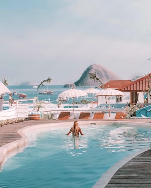 A pool area with lounge chairs and umbrellas, a wooden deck, and a mountain in the background.