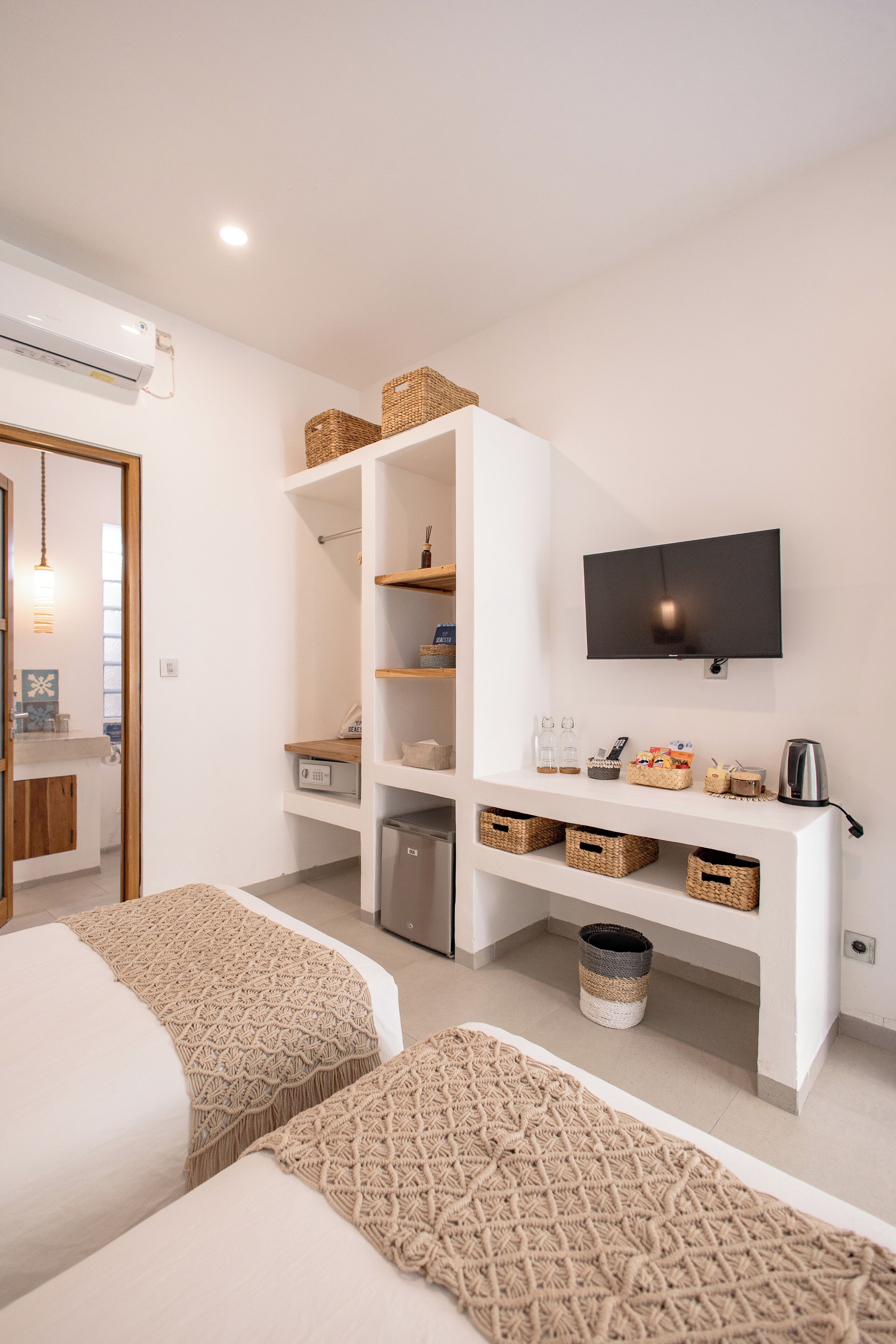 Une chambre d’hôtel moderne dotée d’un grand lit, d’un téléviseur fixé au mur, d’une étagère intégrée avec des paniers et d’une petite kitchenette.