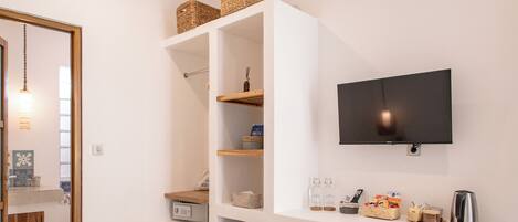 Une chambre d’hôtel moderne dotée d’un grand lit, d’un téléviseur fixé au mur, d’une étagère intégrée avec des paniers et d’une petite kitchenette.