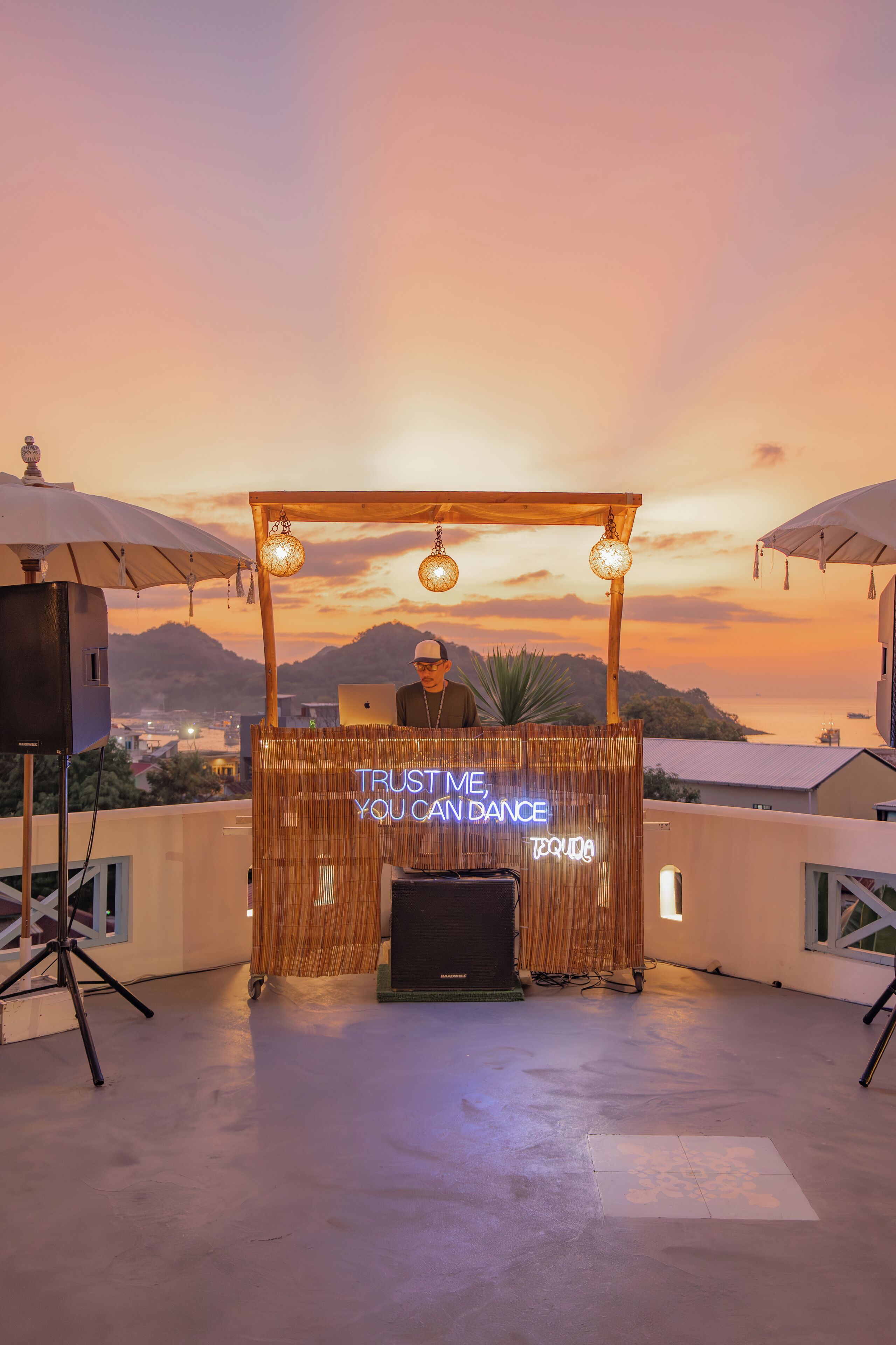 A DJ setup with a neon sign on a balcony overlooking a sunset.