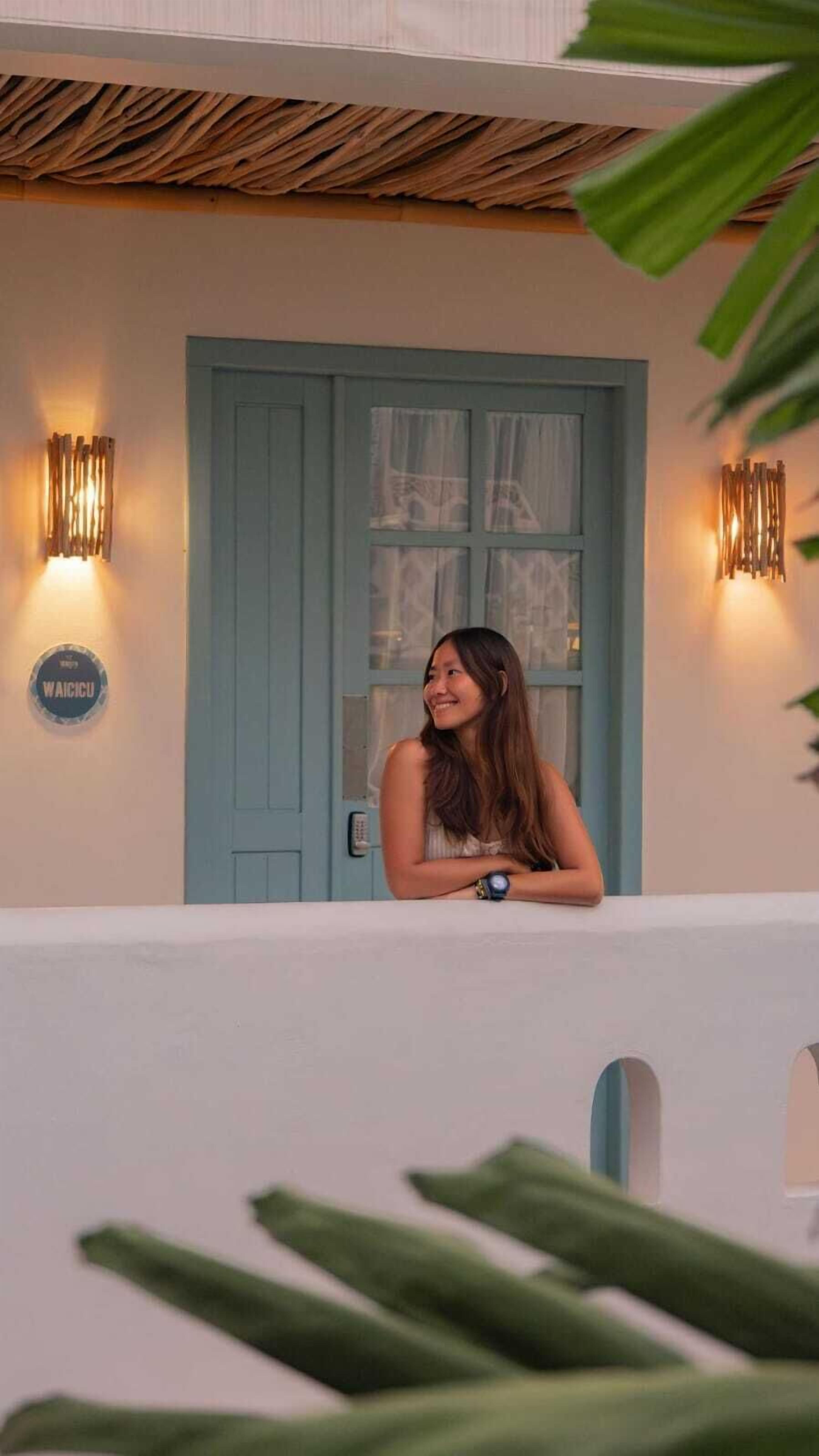 A person standing on a balcony with a blue door and two wall-mounted lights.