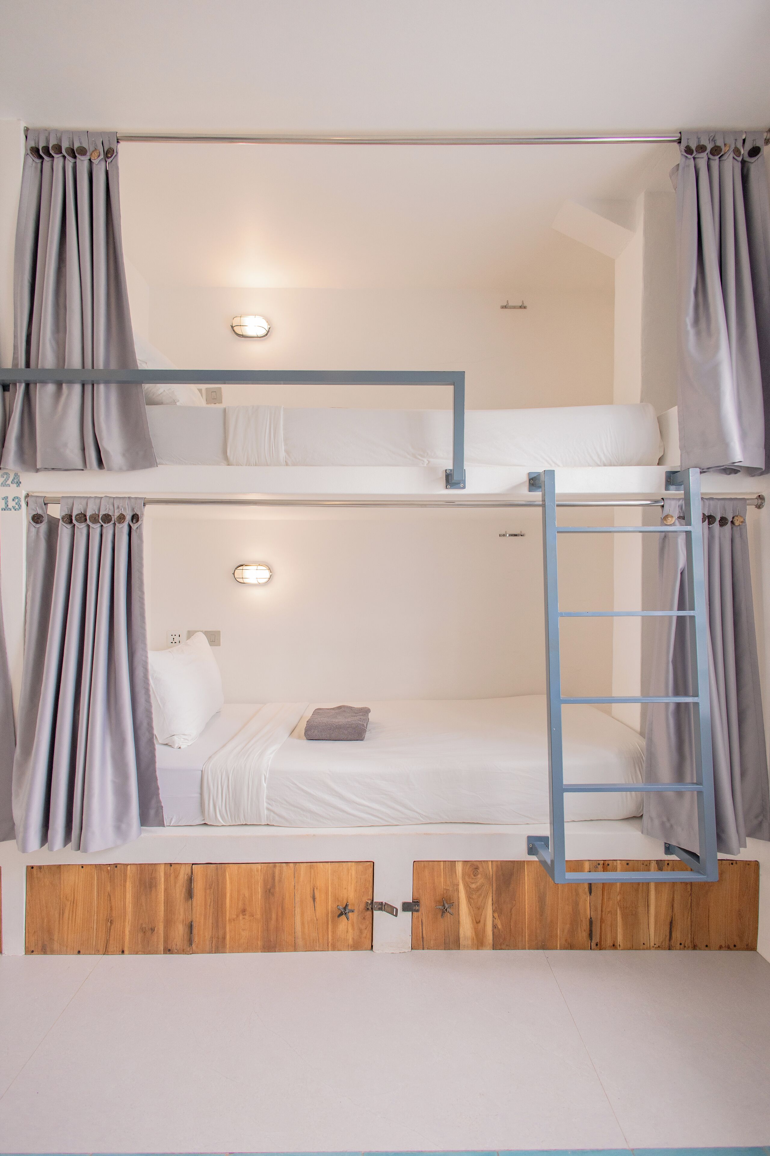 Une chambre avec un lit superposé, une échelle, des rideaux et un panneau en bois en bas.
