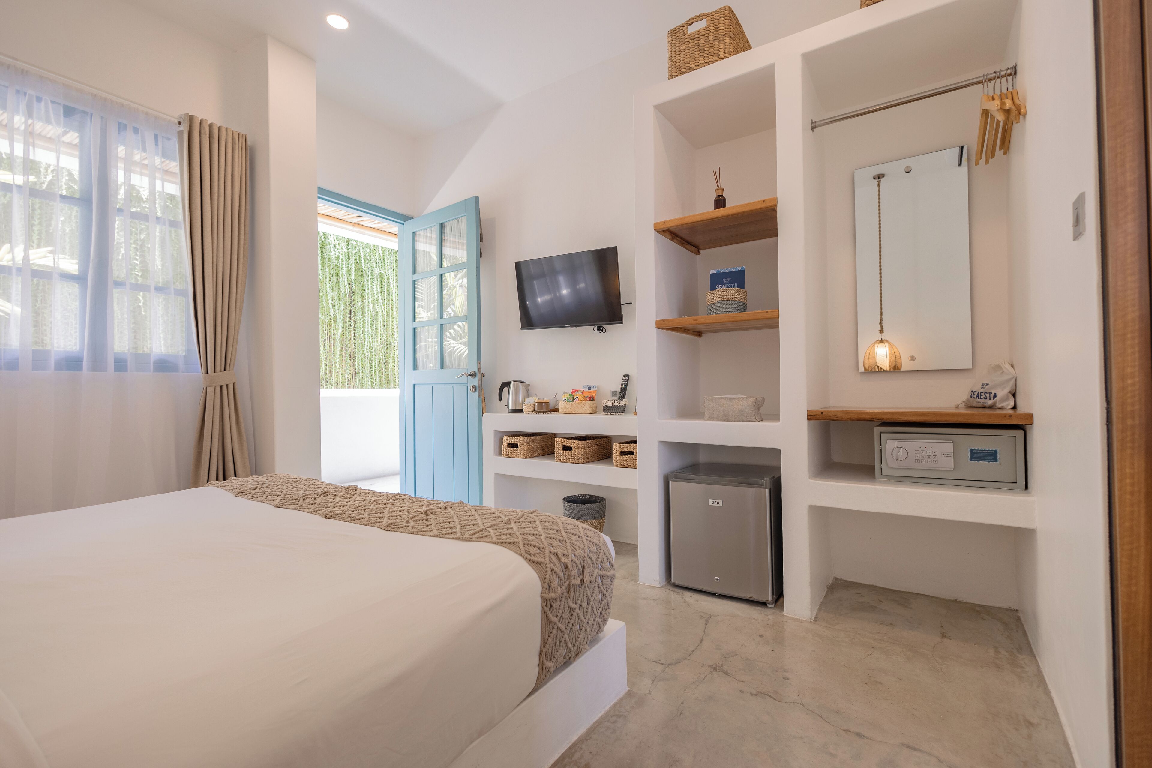 Une chambre à coucher avec un lit, une télévision, un petit réfrigérateur et une salle de bain visible à travers une porte ouverte.