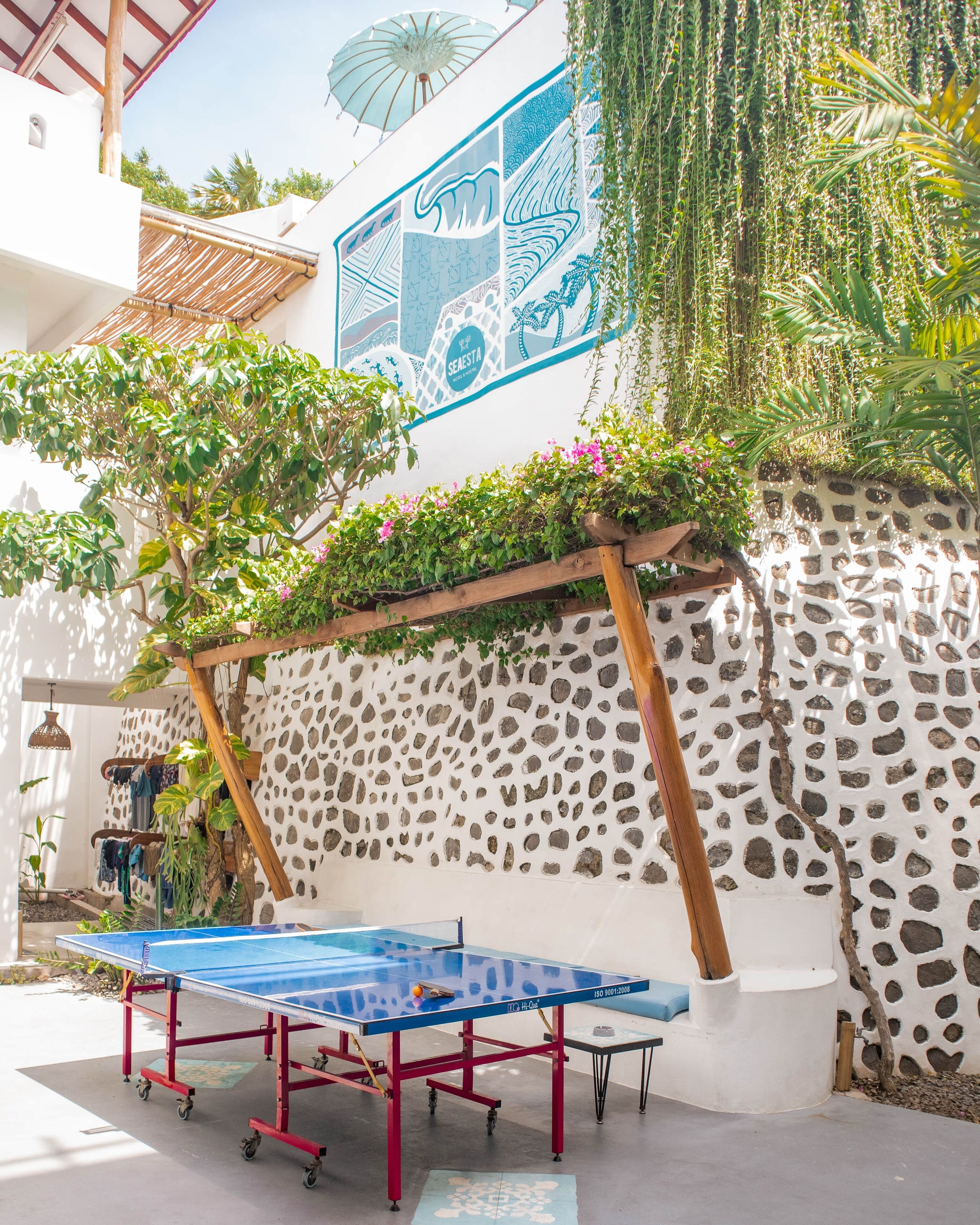 A ping pong table set up outdoors with a stone wall and greenery in the background.
