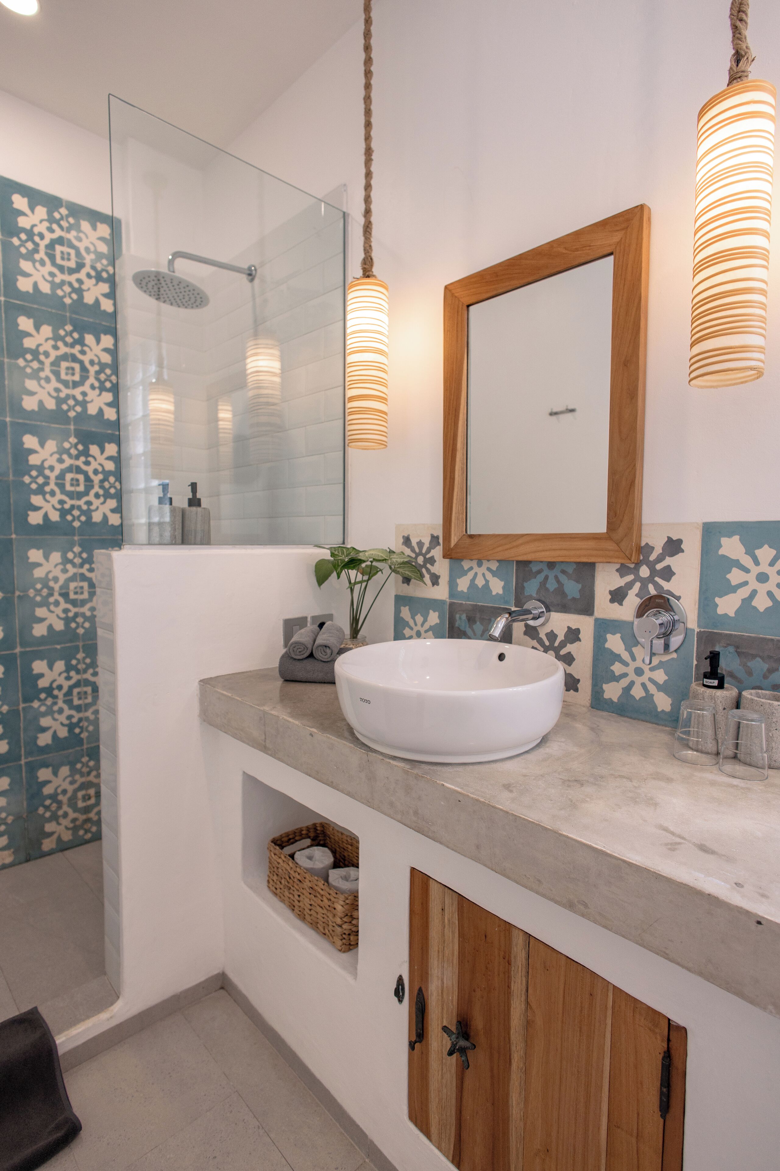 Un baño con cabina de ducha de vidrio, un lavabo blanco, un mueble de madera y azulejos estampados.