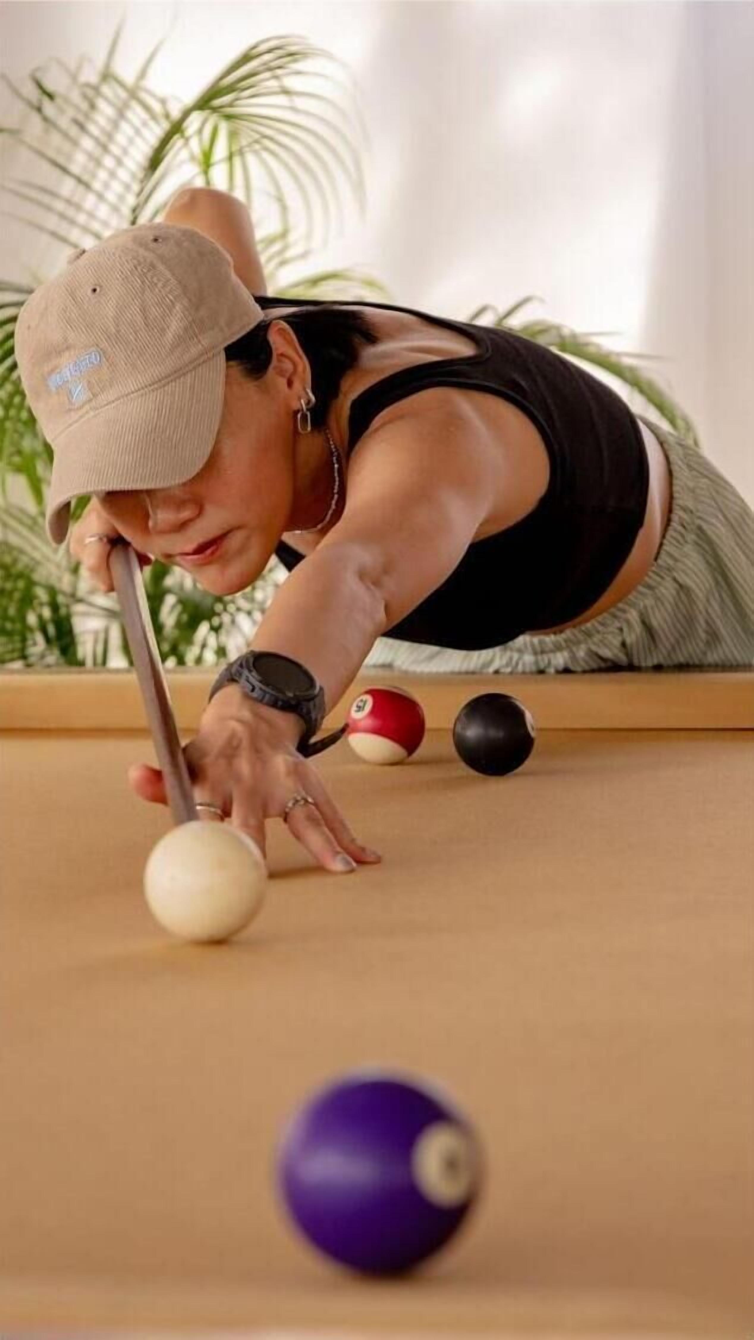 Une personne jouant au billard, penchée au-dessus de la table, tenant un bâton de billard à la main.
