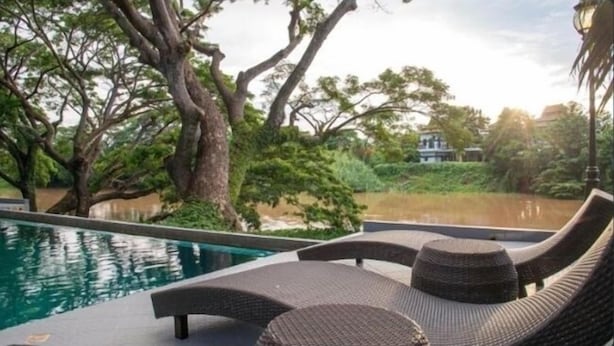 Zona de piscina con sillones de mimbre y vistas al agua y a árboles.
