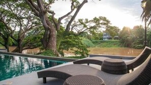 Zona de piscina con sillones de mimbre y vistas al agua y a árboles.