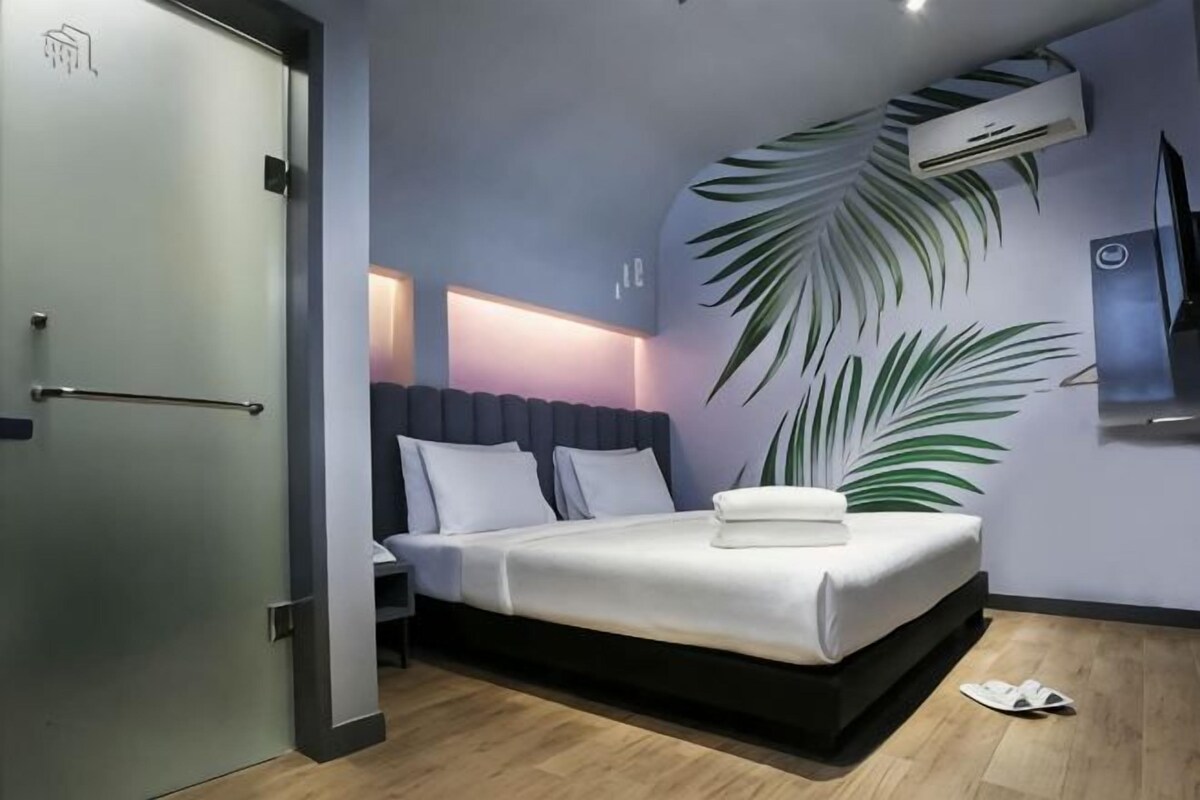 Ett modernt hotellrum med en säng, ett sängbord, en väggmonterad luftkonditioneringsanläggning och en stor växt.