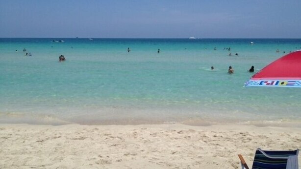 A beach with clear turquoise water, a red umbrella, and a striped beach chair.