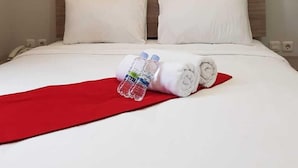 A neatly made bed with white linens, a red throw blanket, and two water bottles. - POD House Pakubuwono - Hostel (Jakarta)