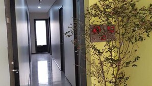 A modern hallway with a yellow accent wall, a potted plant, and a door with a red sign. - POD House Pakubuwono - Hostel (Jakarta)
