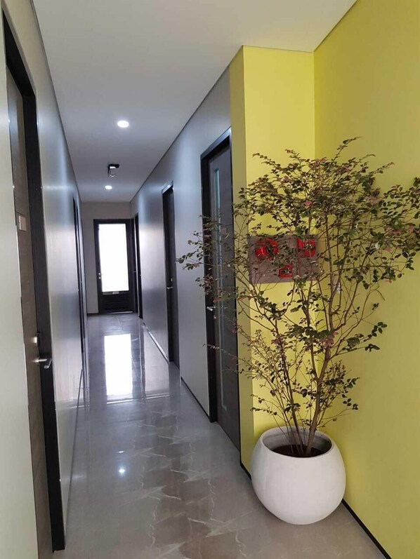 A modern hallway with a yellow accent wall, a potted plant, and a door with a red sign.