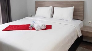 A neatly made bed with white linens, a red throw, and rolled towels. - POD House Pakubuwono - Hostel (Jakarta)