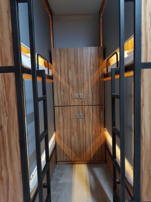 A narrow hallway with wooden paneling and metal frames, leading to a central door with two handles. - POD House Pakubuwono - Hostel (Jakarta)