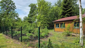 A fenced garden area with a wooden cabin and dense trees in the background. - Cozy wooden cottage with Wi-Fi and feel-good atmosphere (Bohmte)