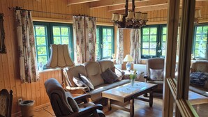 A cozy cabin interior with wooden floors, a sofa, a chair, a coffee table, and a chandelier. - Cozy wooden cottage with Wi-Fi and feel-good atmosphere (Bohmte)