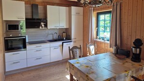 A wooden cabin interior with a kitchen featuring white cabinets, a built-in microwave, a stove, and a dining table with a sunflower tablecloth. - Cozy wooden cottage with Wi-Fi and feel-good atmosphere (Bohmte)