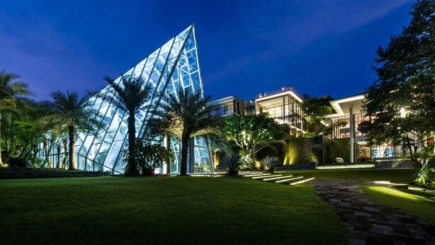 A modern building with a glass pyramid structure, surrounded by well-maintained greenery and a stone pathway.