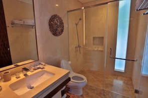 Un baño moderno con ducha de mampara de vidrio, un espejo grande y un inodoro.