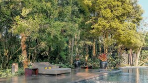 A pool area with a mosaic-tiled hot tub, surrounded by lush greenery and a seating area with cushions.