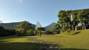 A grassy area with a paved path leading to a building with a pyramid-like structure in the background.