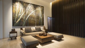 A modern living room with a large abstract painting, a sofa, two ottomans, a coffee table, and a wooden accent wall.