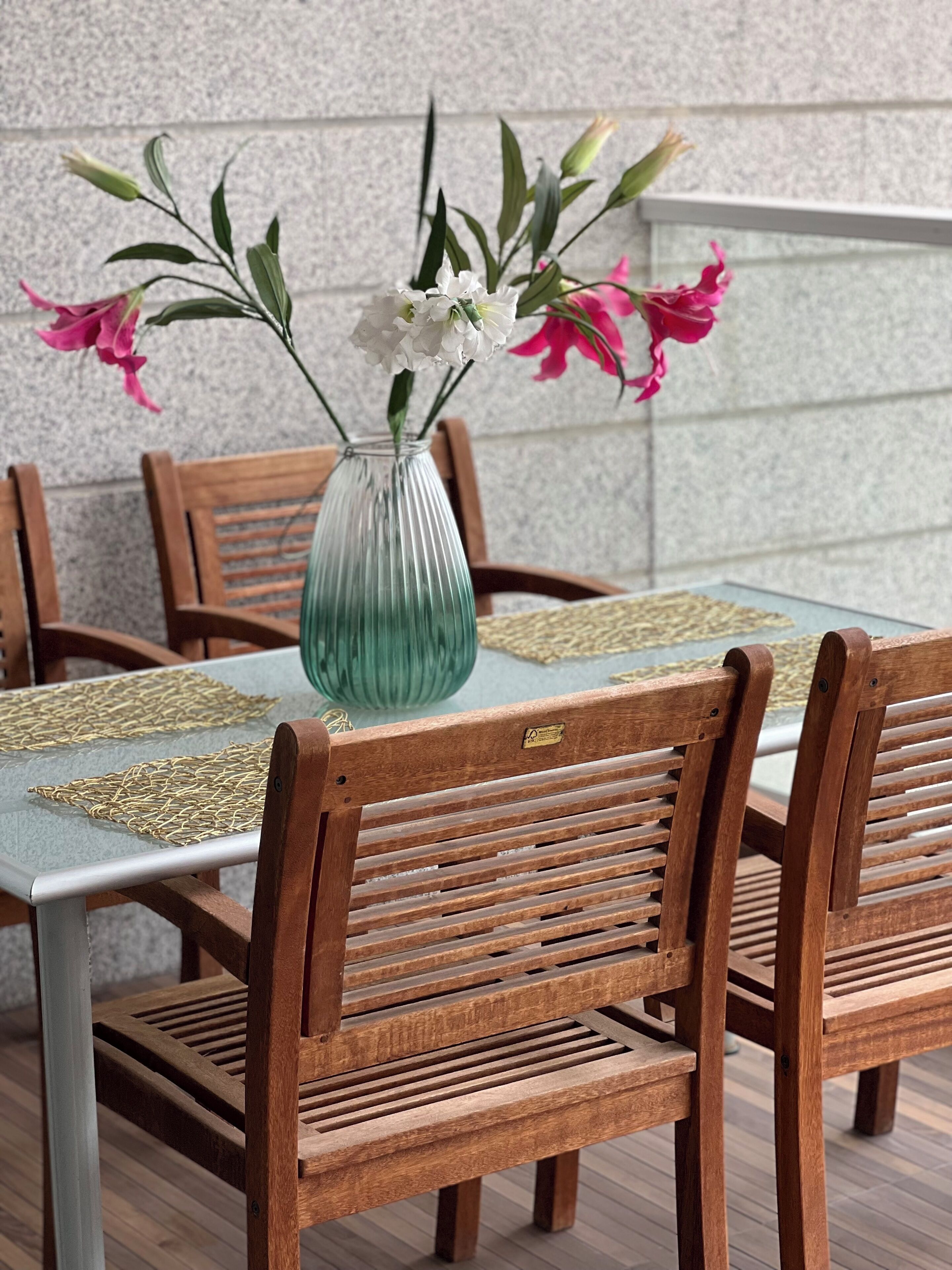 Ein Esstisch mit einer Glaskaraffe mit Blumen, Holzsesseln und gewebten Tischsets.