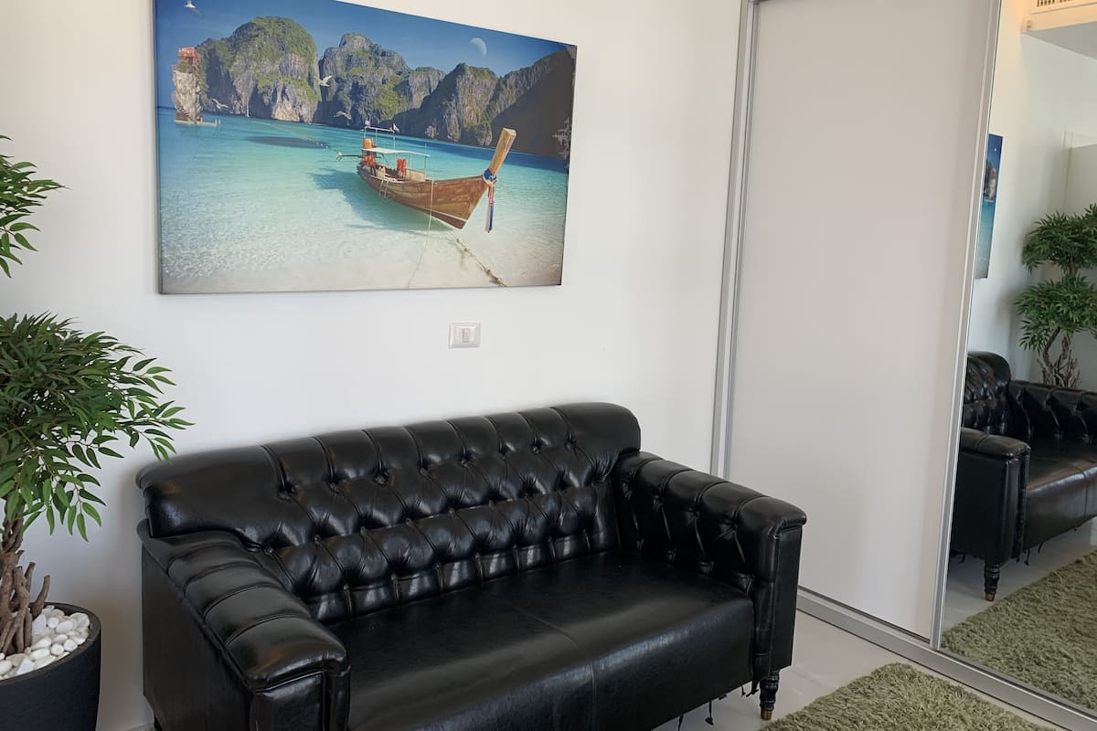 Ein schwarzes Ledersofa, ein Gemälde mit einem Boot am Strand und ein Blumentopf.