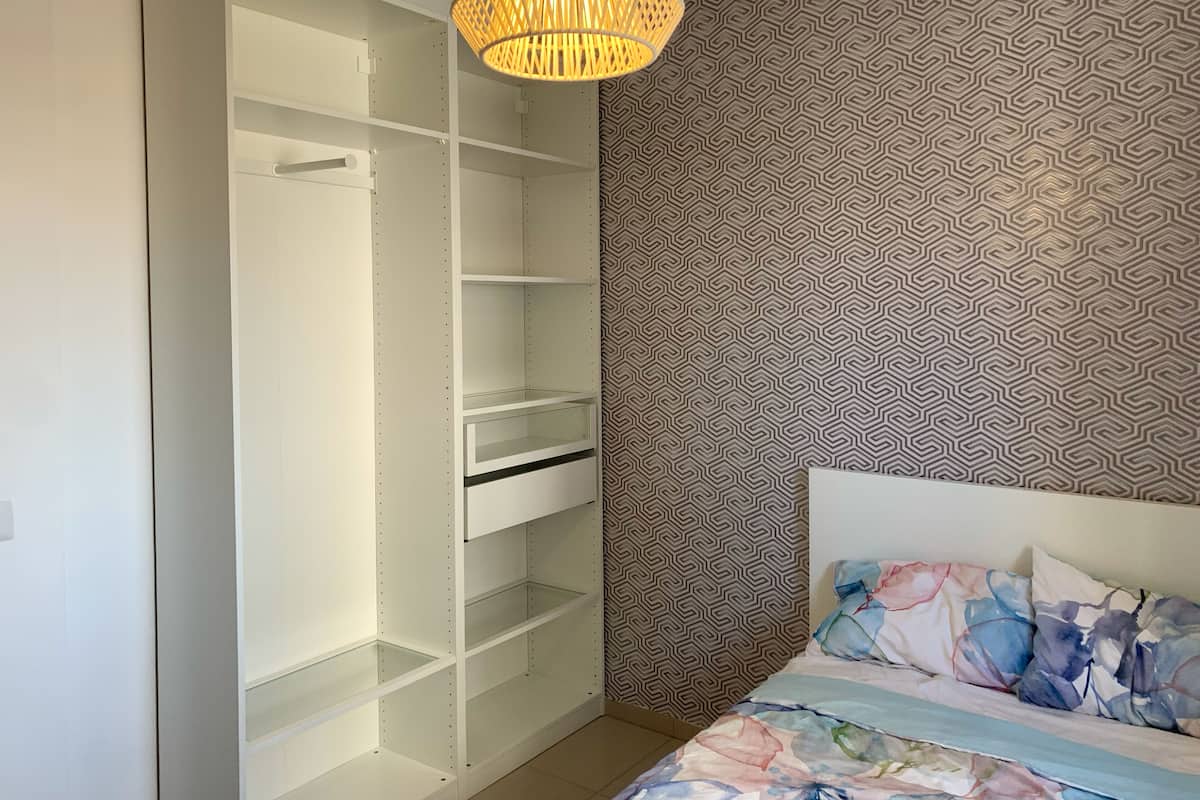Ein Schlafzimmer mit einem Bett, einer Wand mit Muster und einem weißen Kleiderschrank mit Regalen.