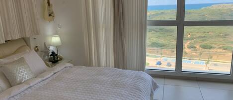 Un dormitorio con cama, cortinas, una guitarra, una mesita de noche y vistas de un paisaje a través de un ventanal amplio.