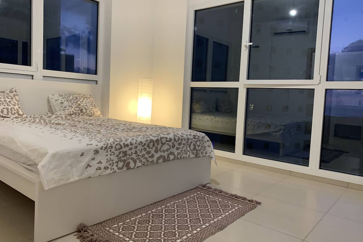 Ein Schlafzimmer mit einem Bett, einem gemusterten Teppich und großen Fenstern.