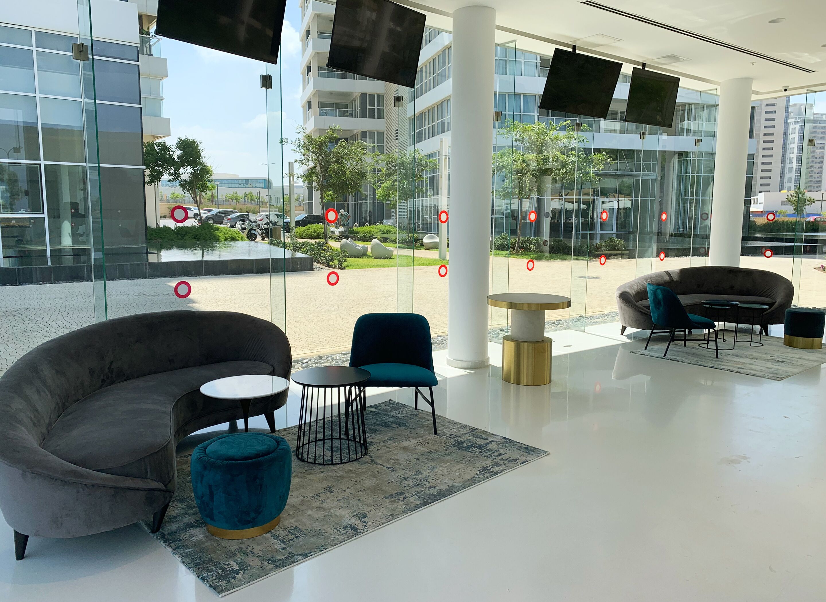 A modern indoor space with a glass wall offering a view of a street and buildings. There are two sofas, a small round table, and a blue chair.