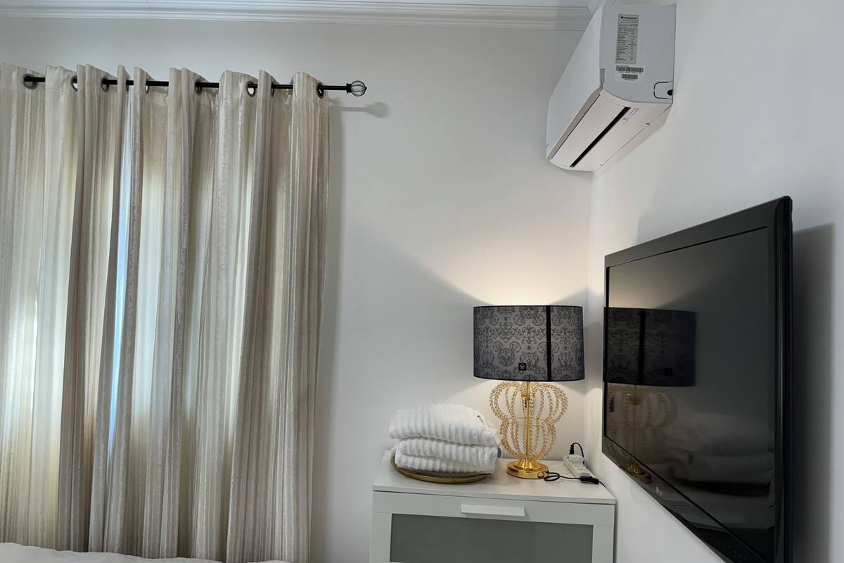 Ein Schlafzimmer mit einem Bett, einem Fernseher, einer Lampe und einer Klimaanlage.