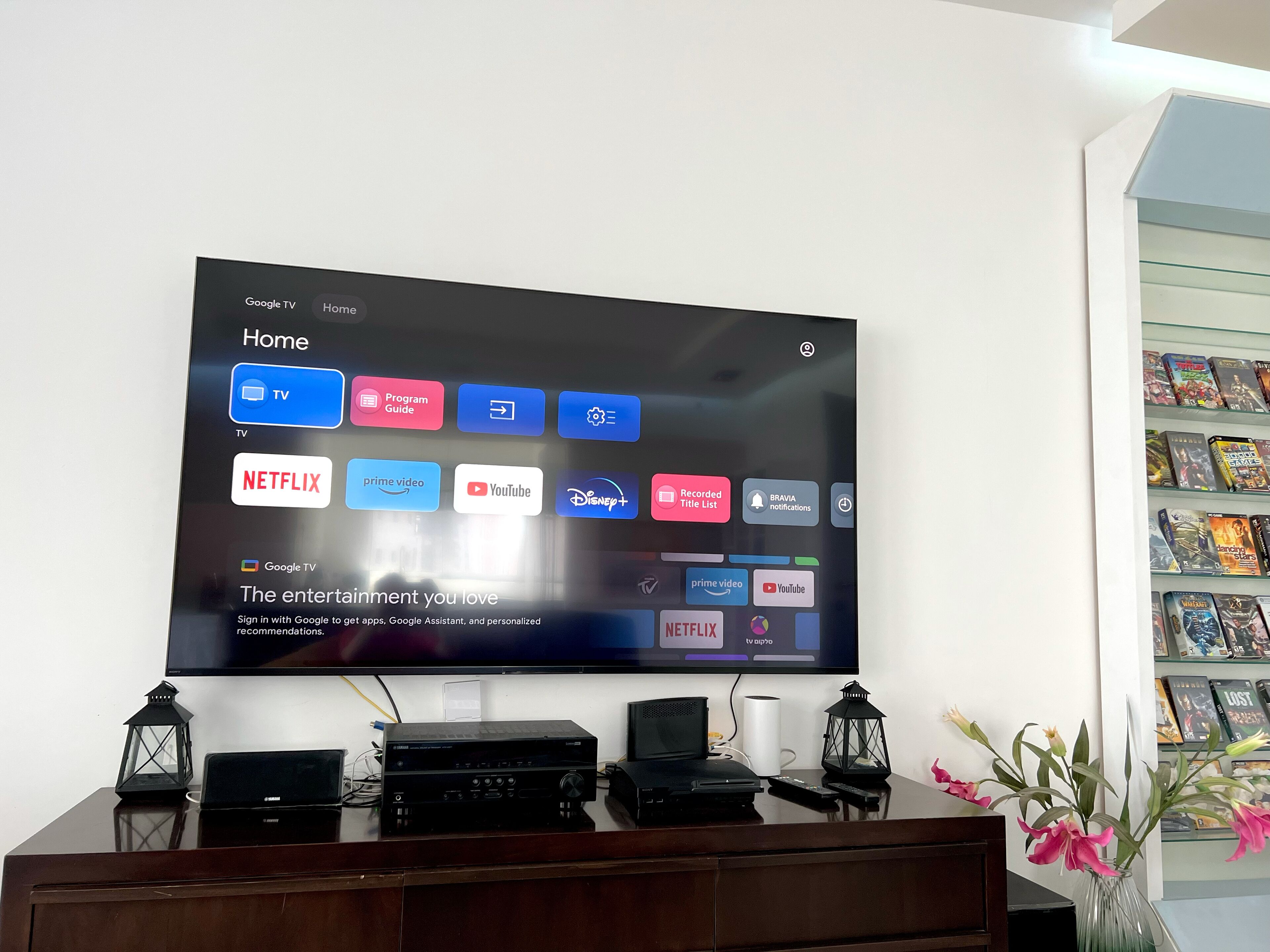 A flat-screen TV mounted on a wall displaying a Google TV interface with various streaming service icons.