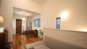 A living room with a sofa, a dining table with chairs, a coffee maker, and a plant. - Aguri Home (Osaka)