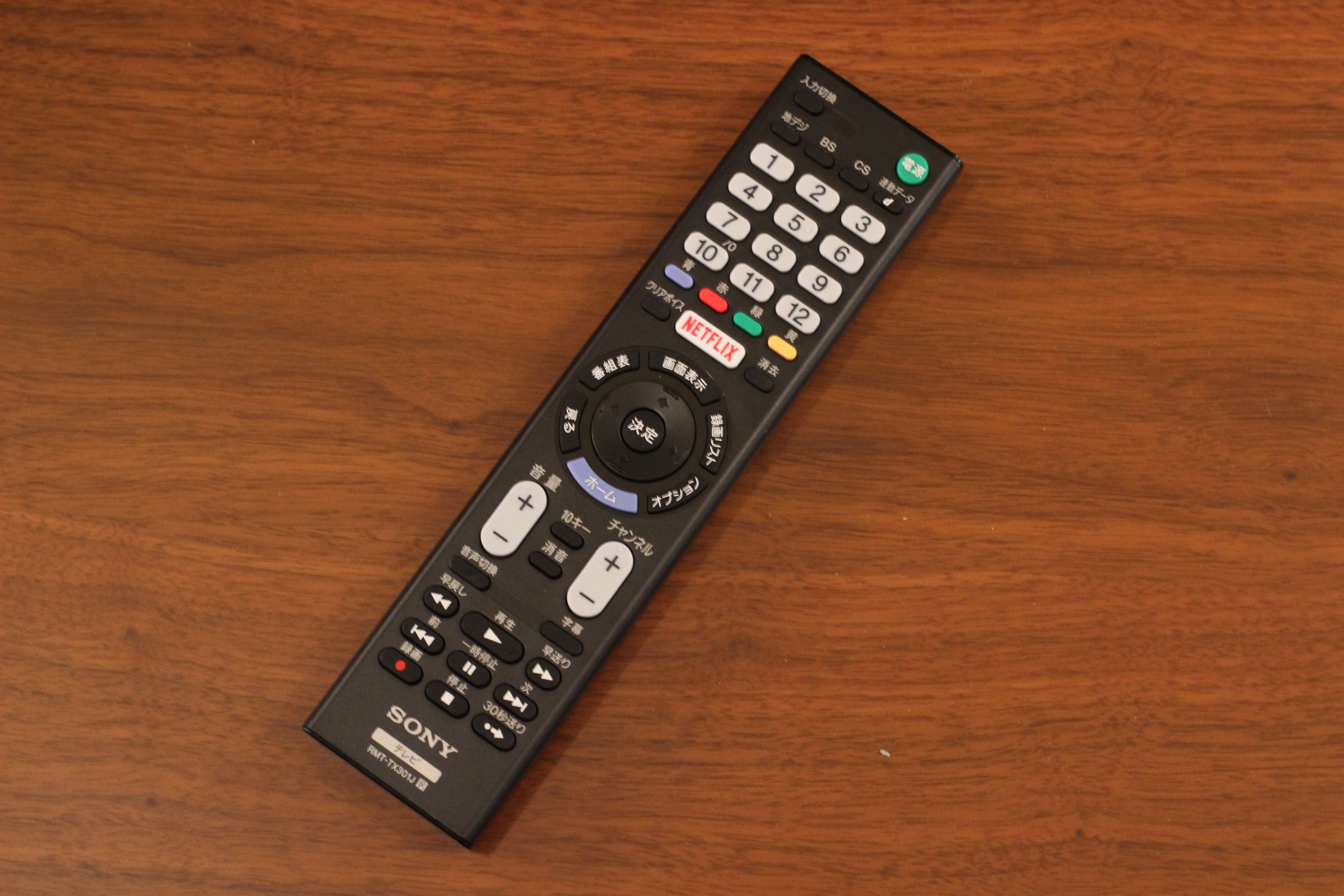 A black Sony remote control with multiple buttons and a circular navigation pad, placed on a wooden surface.