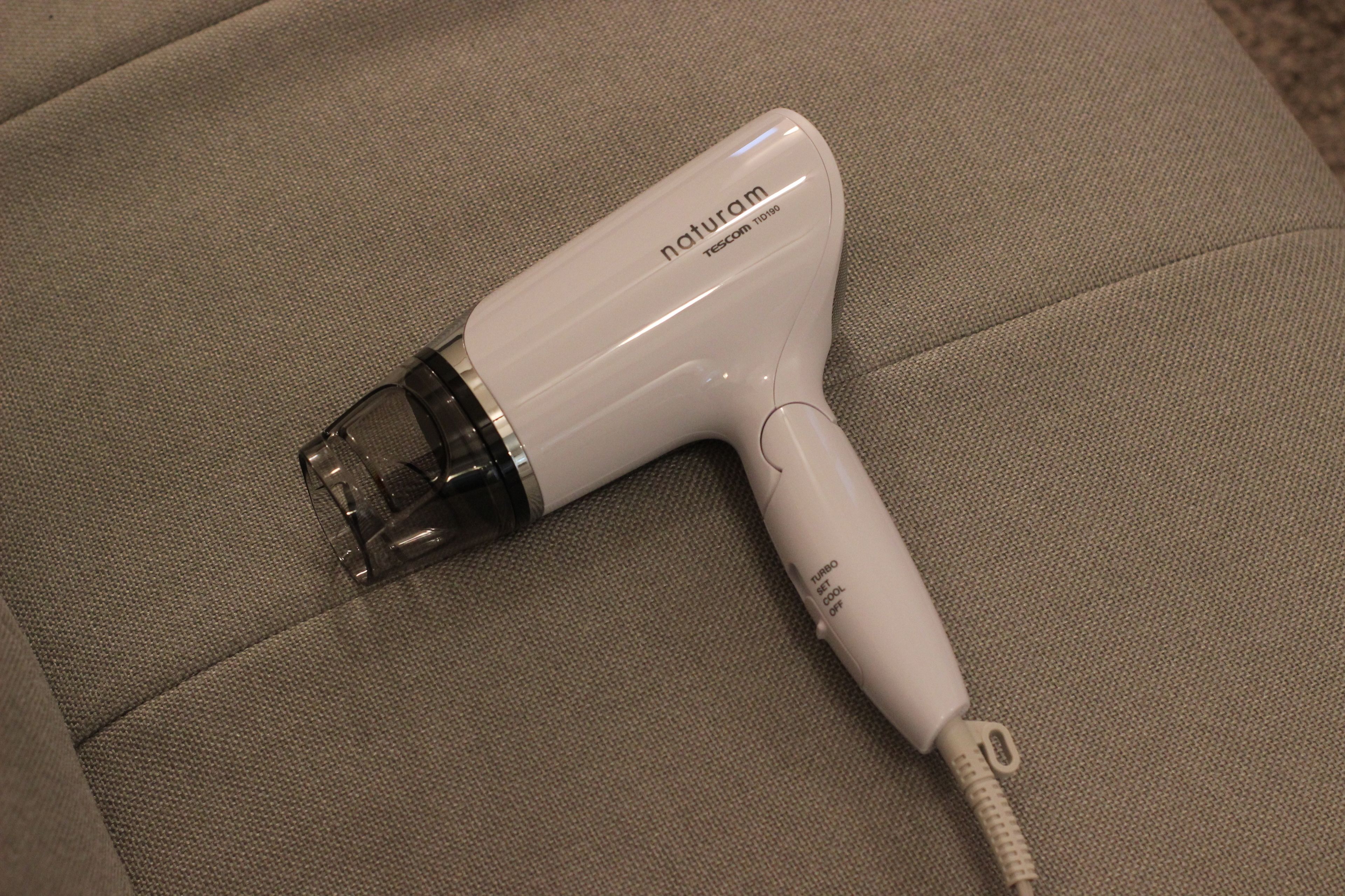 A white hair dryer with the brand name 'naturam' and model 'TESCOM 1100' on a beige couch.