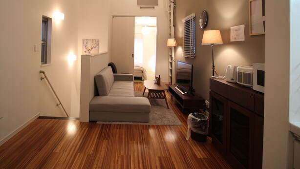 A compact living space with a sofa, a small table, a TV, and a microwave. - Aguri Home (Osaka)