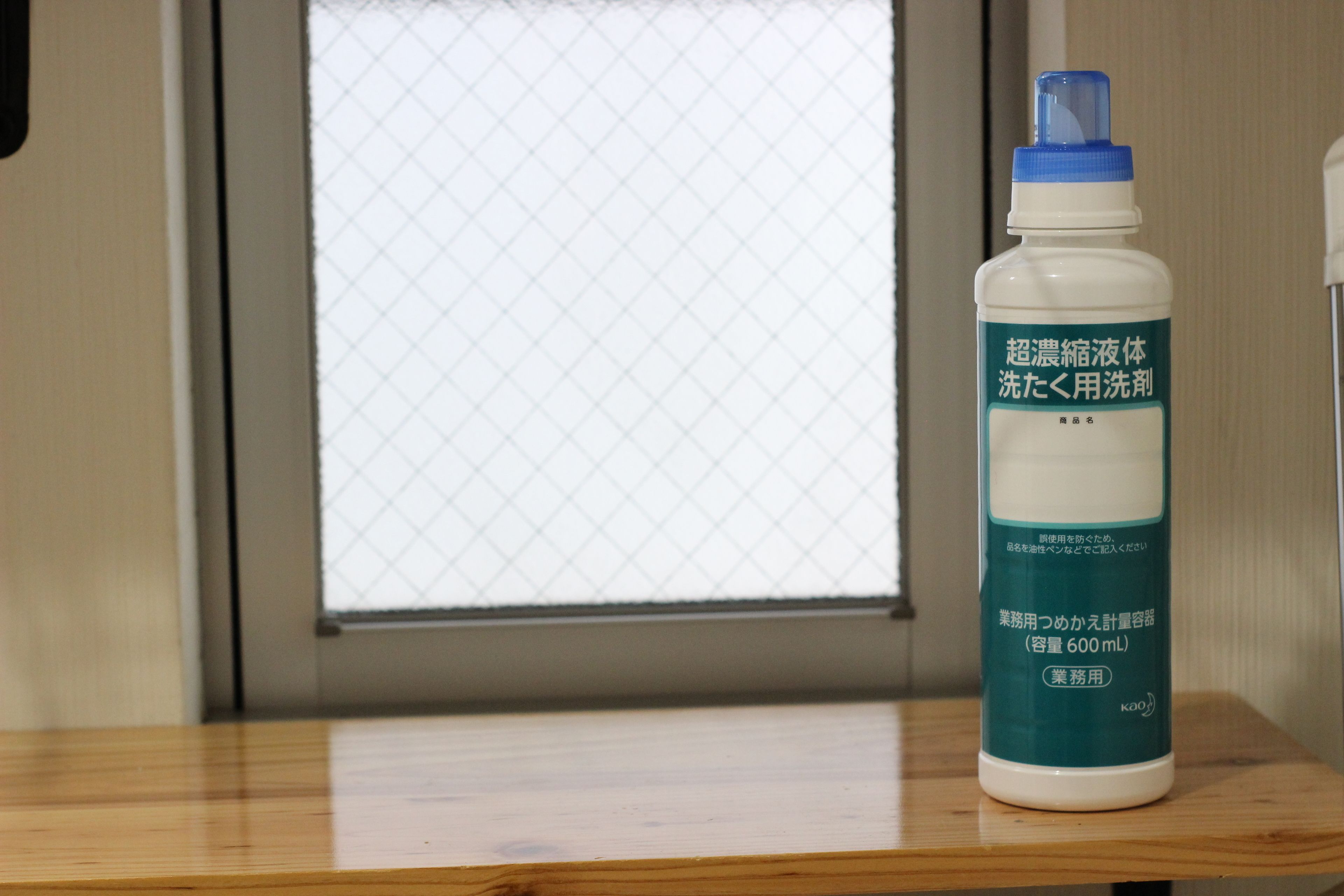 A bottle of liquid on a wooden surface near a window.