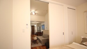A bedroom with a bed, a small seating area, and a kitchenette in the background. - Aguri Home (Osaka)