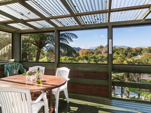 A covered outdoor seating area with a table and chairs, overlooking a scenic landscape with trees and a body of water.