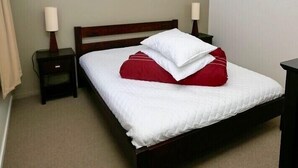 Una cama bien hecha con ropa de cama blanca y roja, un cabecero de madera y dos mesitas de noche con lámparas.